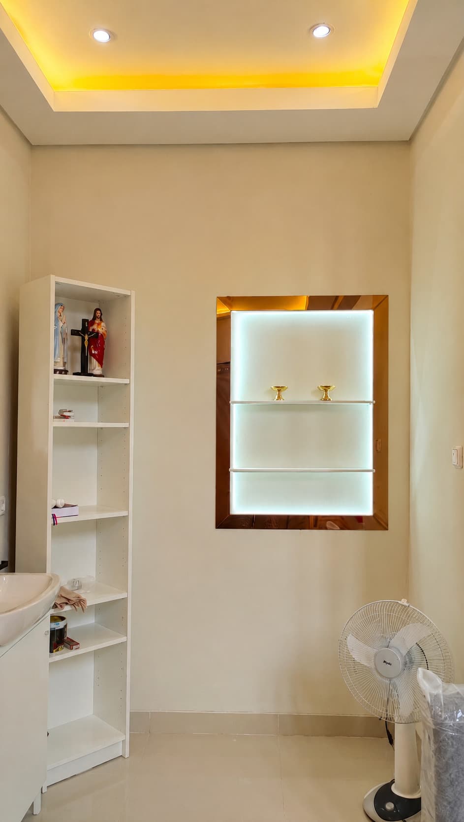 Backlit white wall niche framed in rosegold stainless, holding two brass candlesticks on a glass shelf