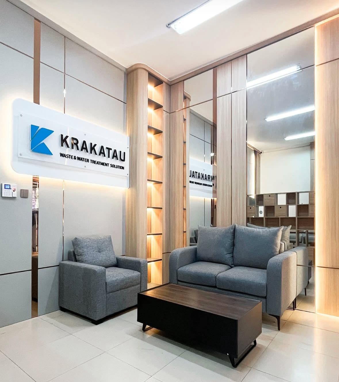 Krakatau office lobby: light timber wall panels and mirrors lined with stainless, a grey sofa, and backlit shelving