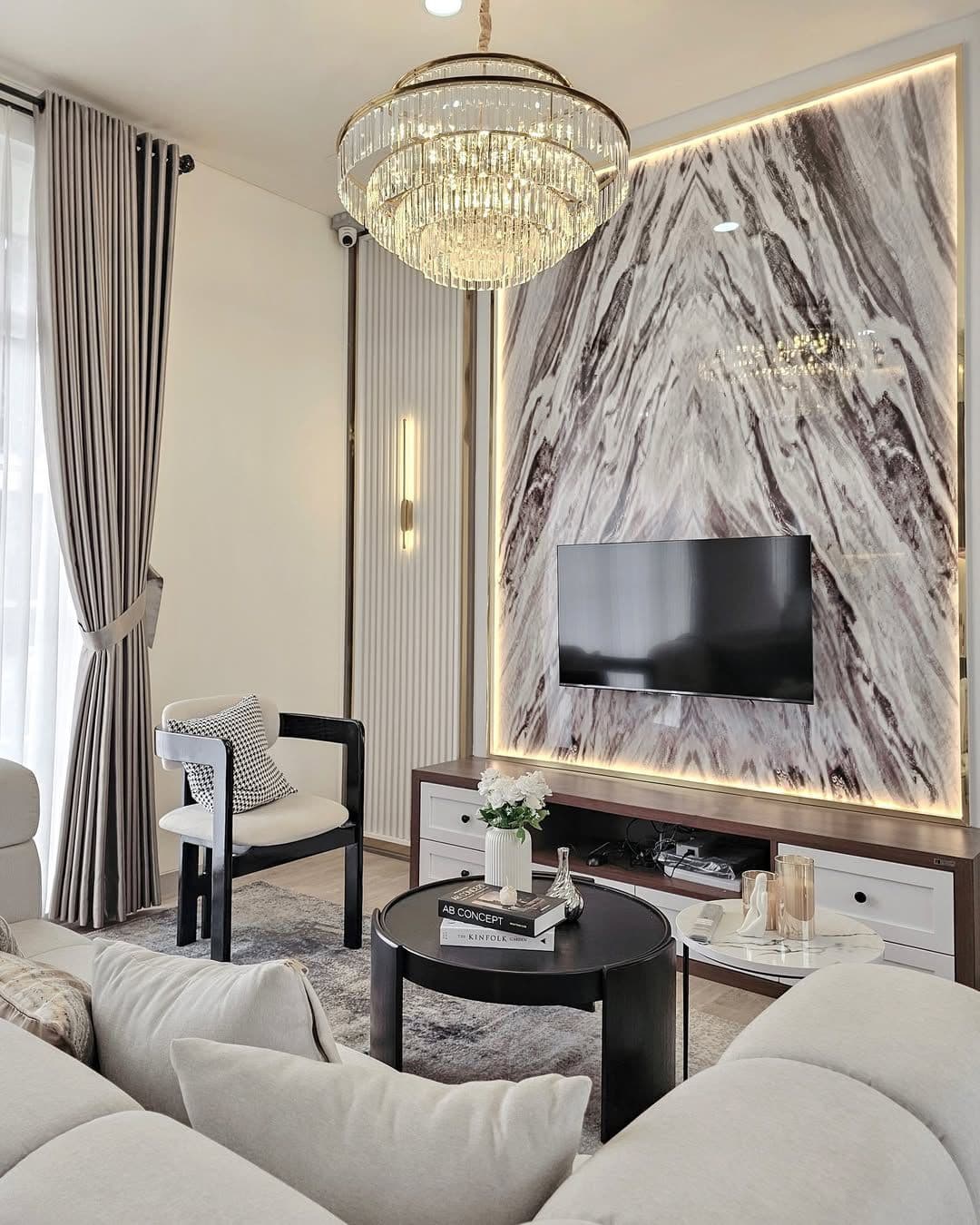 Family room with a marble TV wall framed in gold stainless with hidden lighting, a crystal chandelier, and a cream sofa