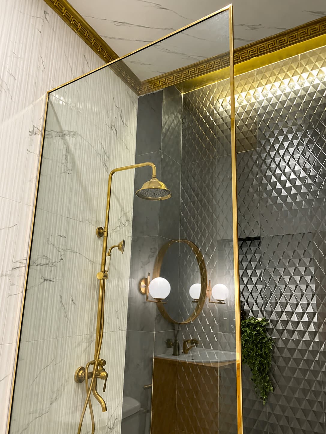Bathroom divided by gold-framed glass, with white marble on one wall and diamond-patterned stainless on the other